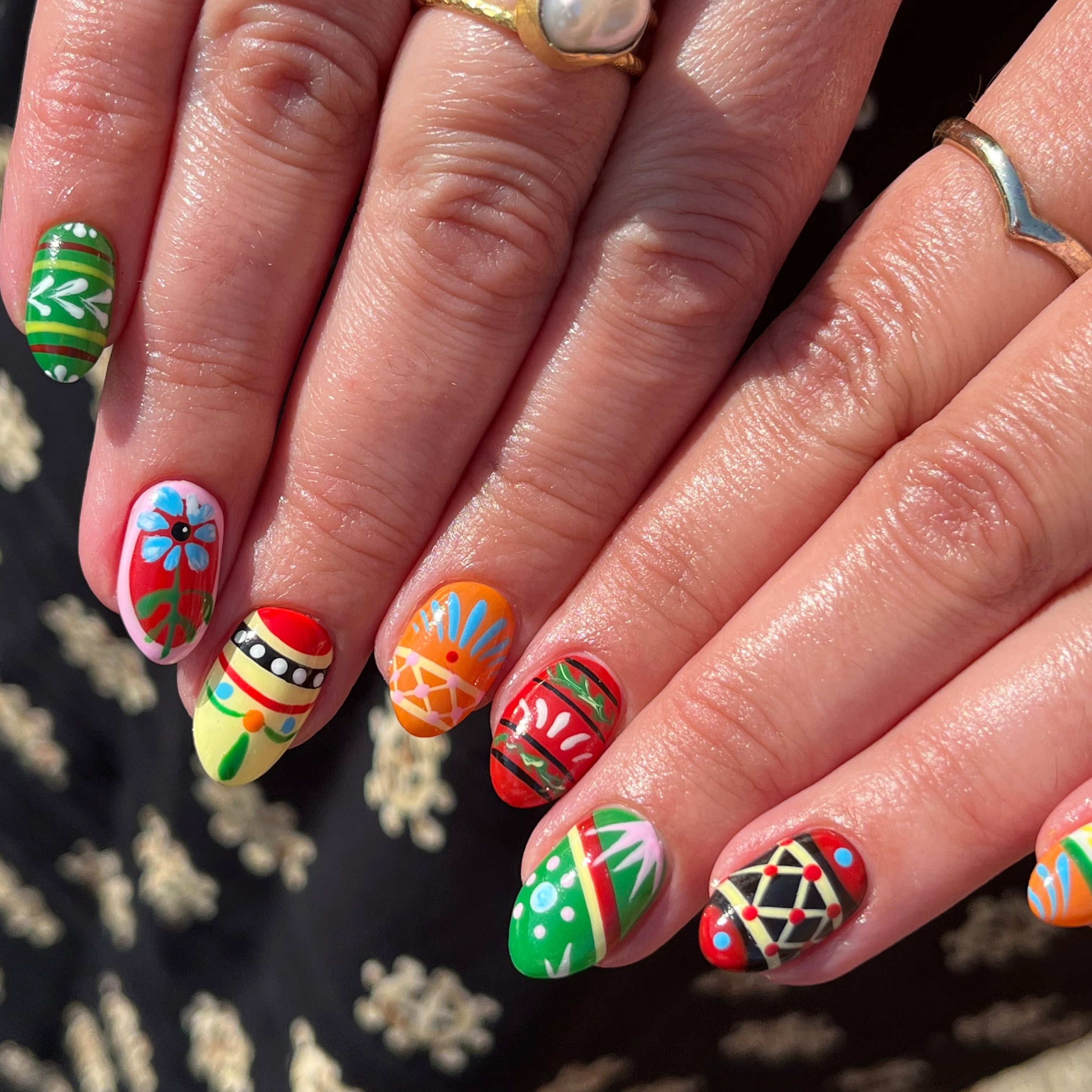 Close-up of hands with colorful nail art on a patterned fabric background